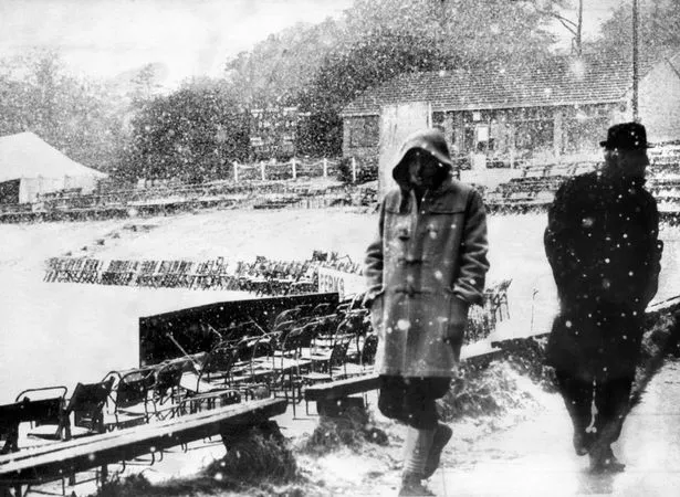 Two men walk around a cricket pitch during the snowfall in June 1975